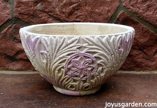 White and pink ceramic pot sitting outside on ground.