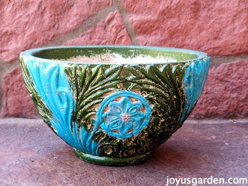 Freshly painted blue and green decorative pot sitting outside on the ground. 