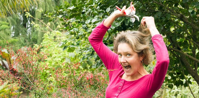 Nell Foster in a bright pink top holding a pair of felco pruners as if she is going to cut her hair 