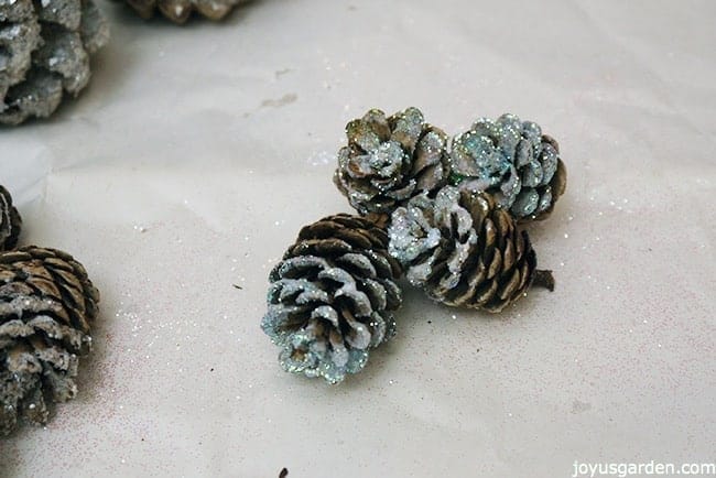 pine cones glittered with iridescent glitter sit on a piece of white paper