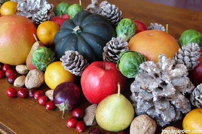 a christmas table centerpiece with fruits vegetables nuts & glitter pinecones