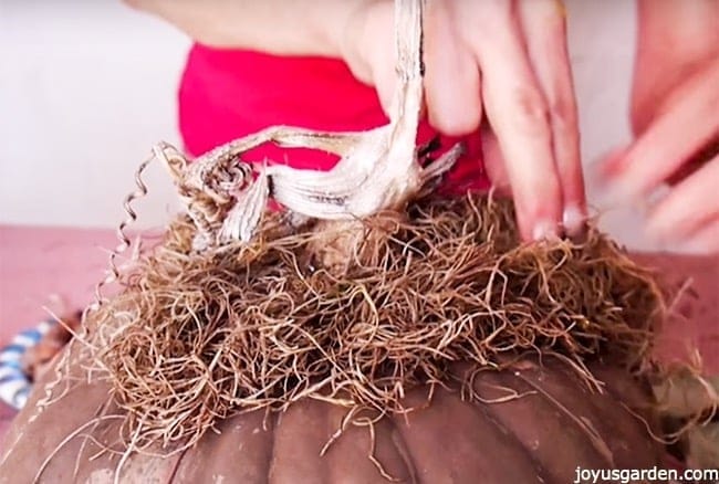 spanish moss is being glued onto the top of a brown pumpkin