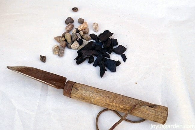 A mini gardening trowel sits below a small pile of pebbles & a small pile of charcoal