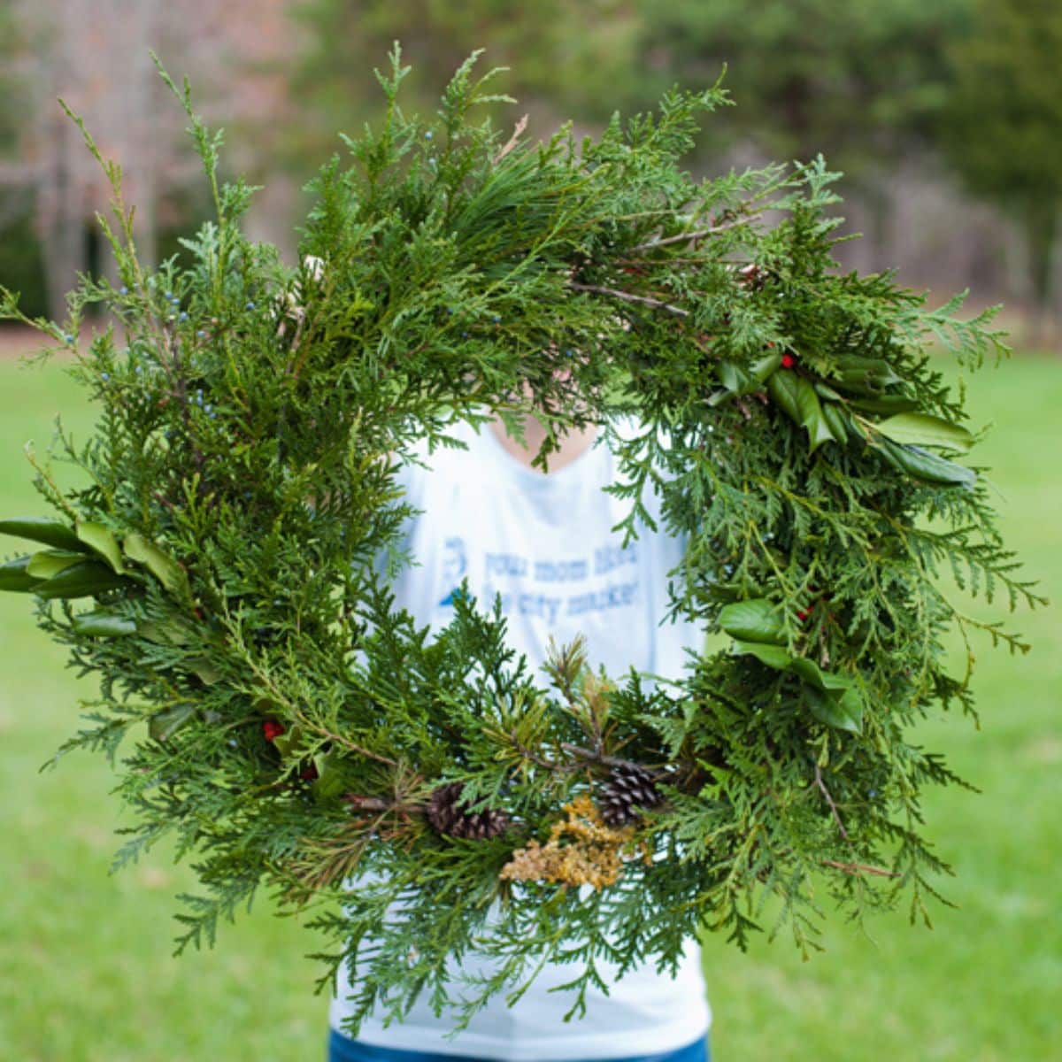 Evergreen Wreath with woman holding it up standing outdoors