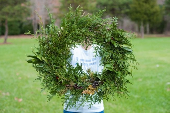 a round evergreen wreath being hold by a woman