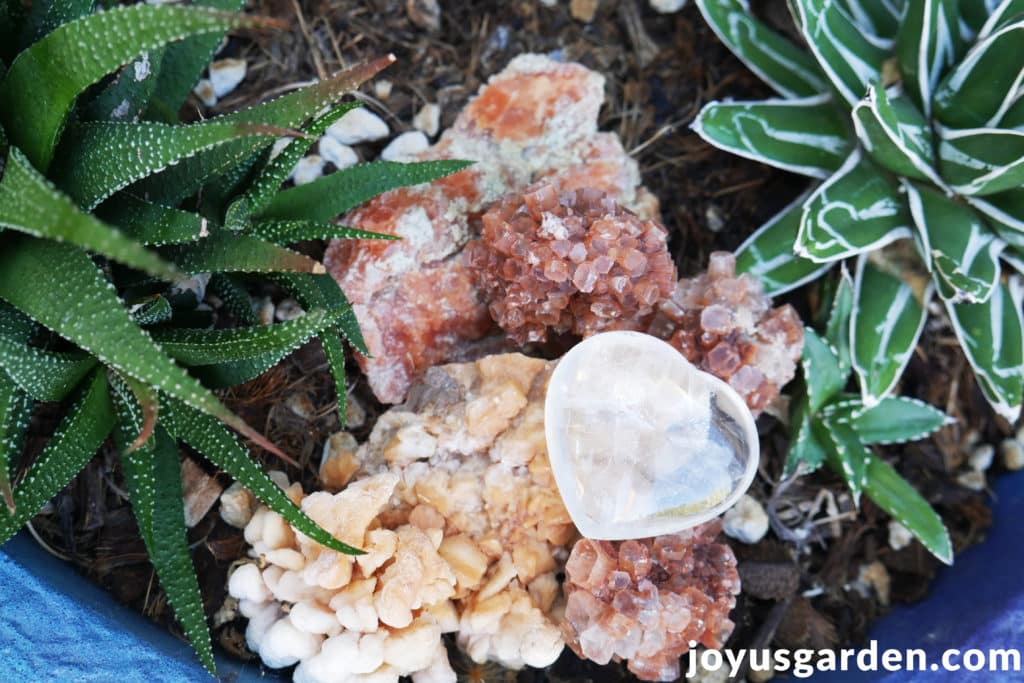 a crystal heart sits in a blue planter with succulents