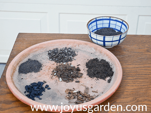 a large terra cotta saucer sits on a table with 6 different soils & amendments in it a blue & white bowl sits behind it