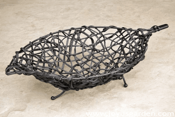 a modern black oval-shaped basket with wire feet sits on a cement patio