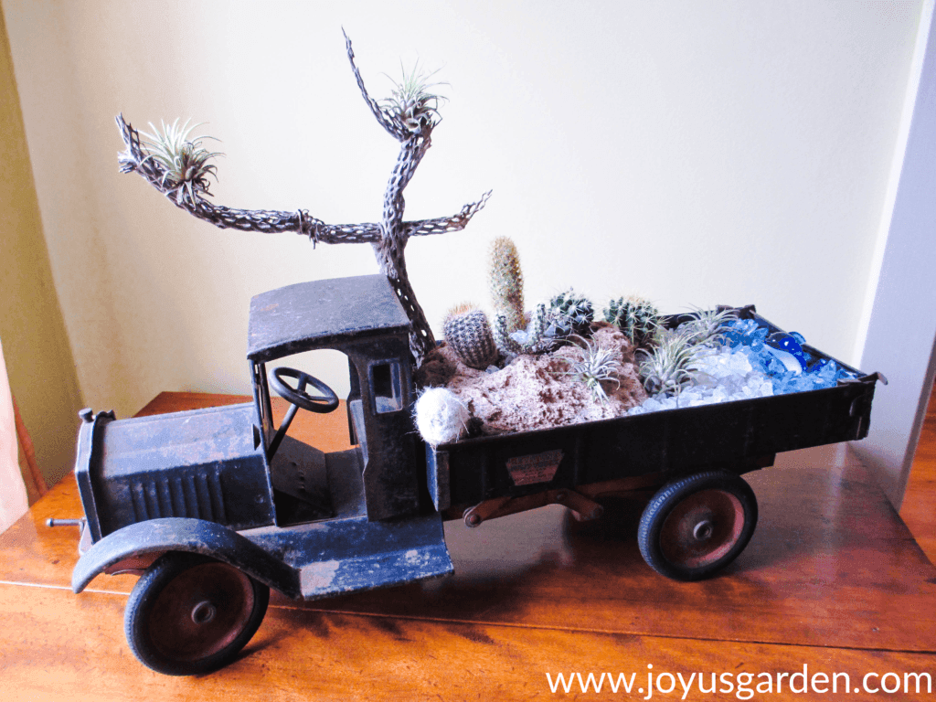 a dish garden with cacti, air plants, pumice stone & glass chips created in an antique dump truck sits on a table