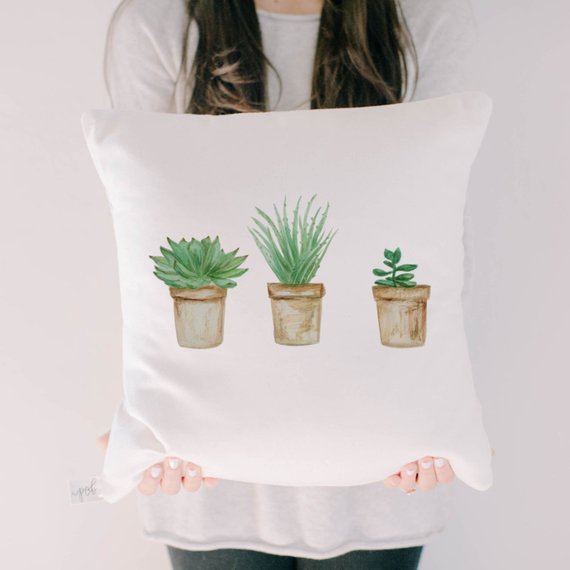 a white throw pillow with 3 succulents in pots on it