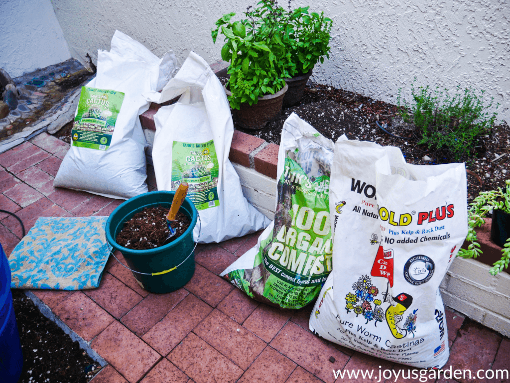 4 bags of soil mix & amendments lined up on a brick walkway