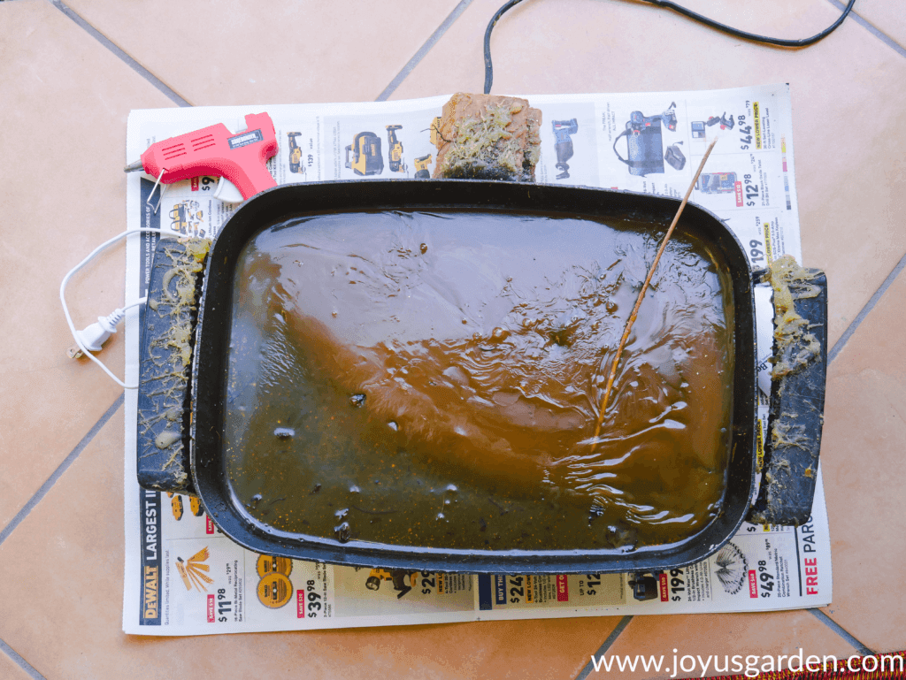 close up of an old electric skillet filled with dry hot glue a small glue gun sits next to it