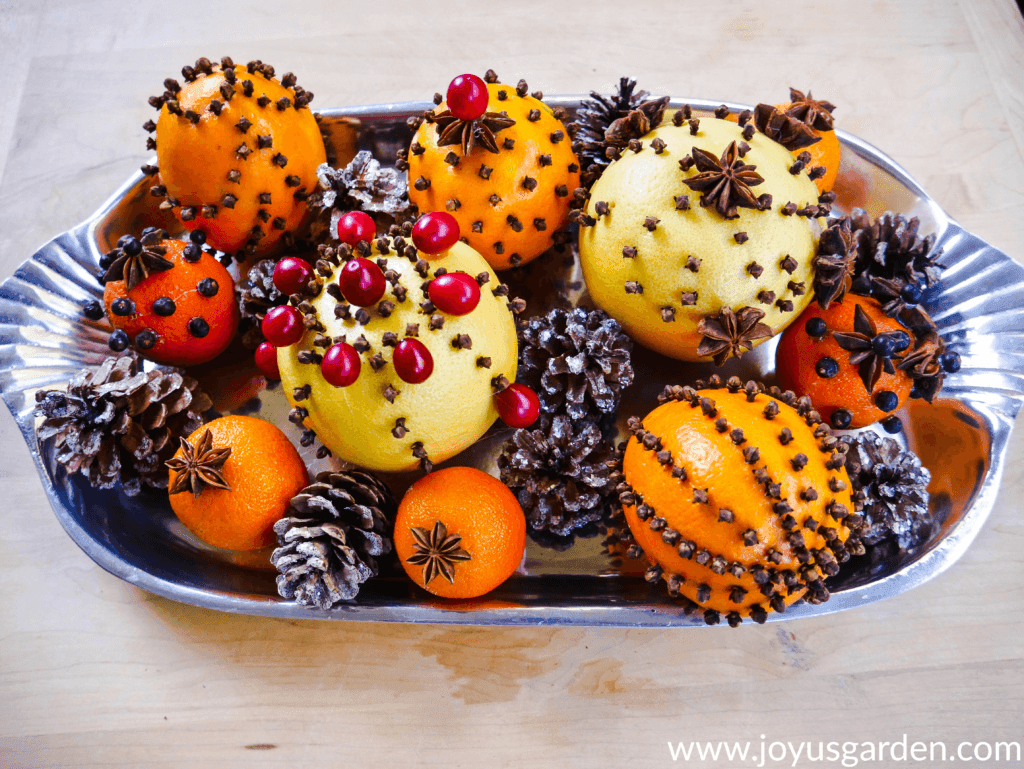 a silver tray is filled with citrus fruits adorned with cloves star anise star anise & cranberries along with glittered pine cones 