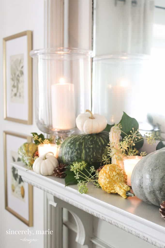 a mantle piece decorated for fall in greens & whites with pumpkins eucalyptus pine cones & candles