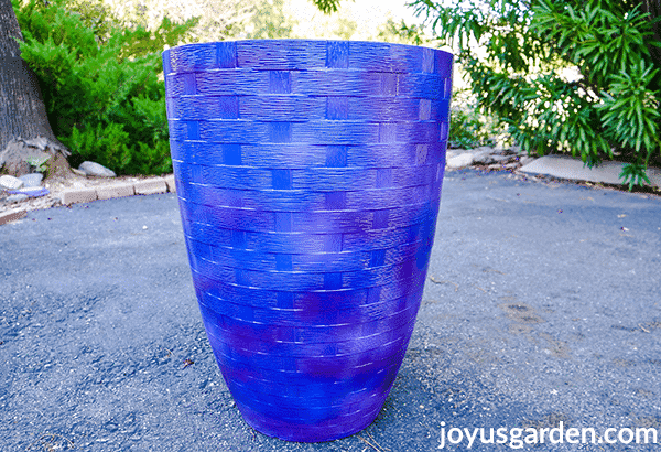 a tall blue vase type pot sits in a driveway