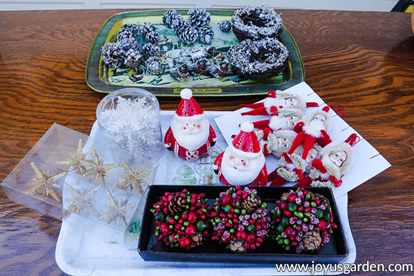 2 trays full of christmas ornamentation sit on a wooden table