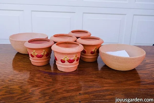2 terra cotta bowls & 5 terra cotta pots painted with red & gold sit on a table