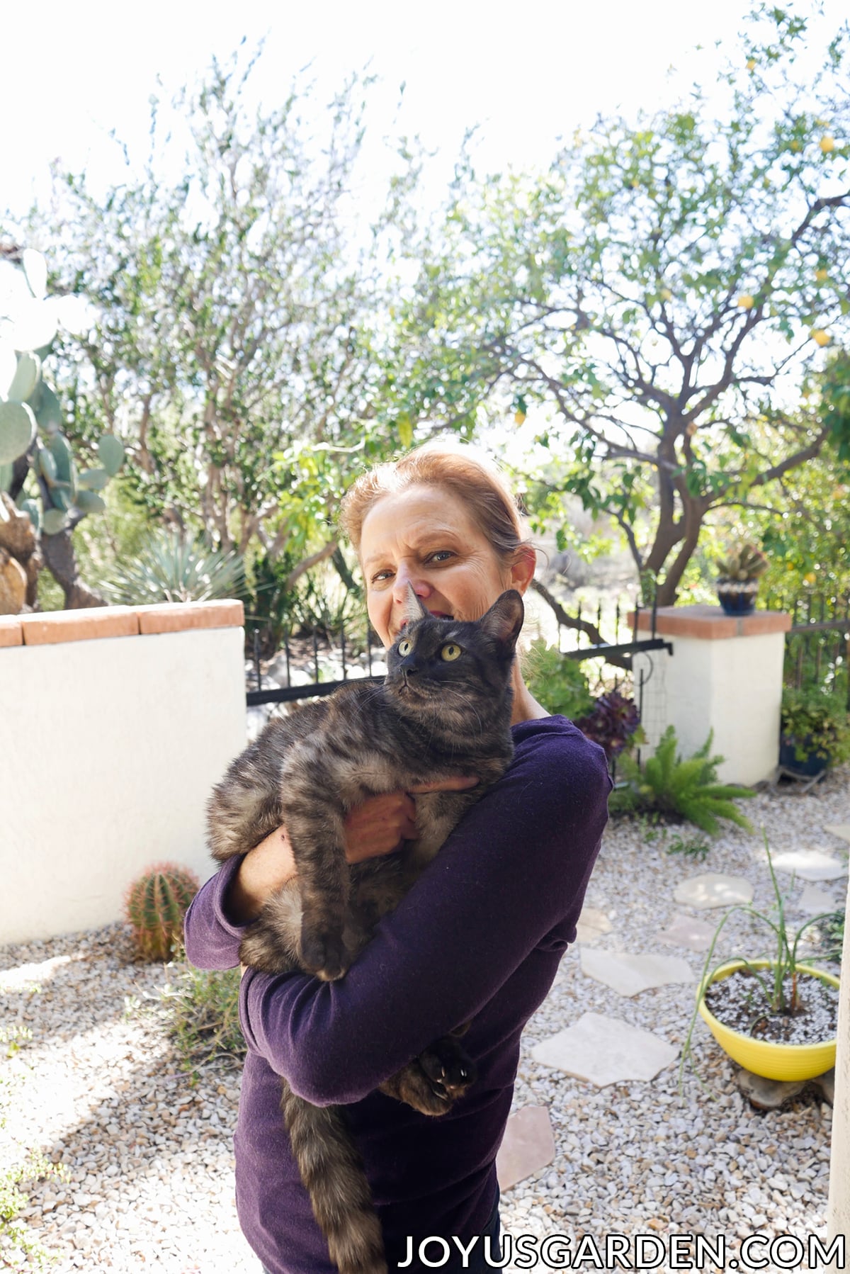 nell foster holds her grey striped kitty Riley in her garden