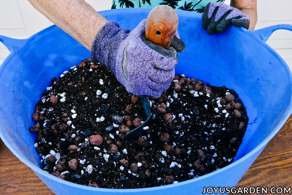 a hand holding a trowel blends soil mix in a blue tub