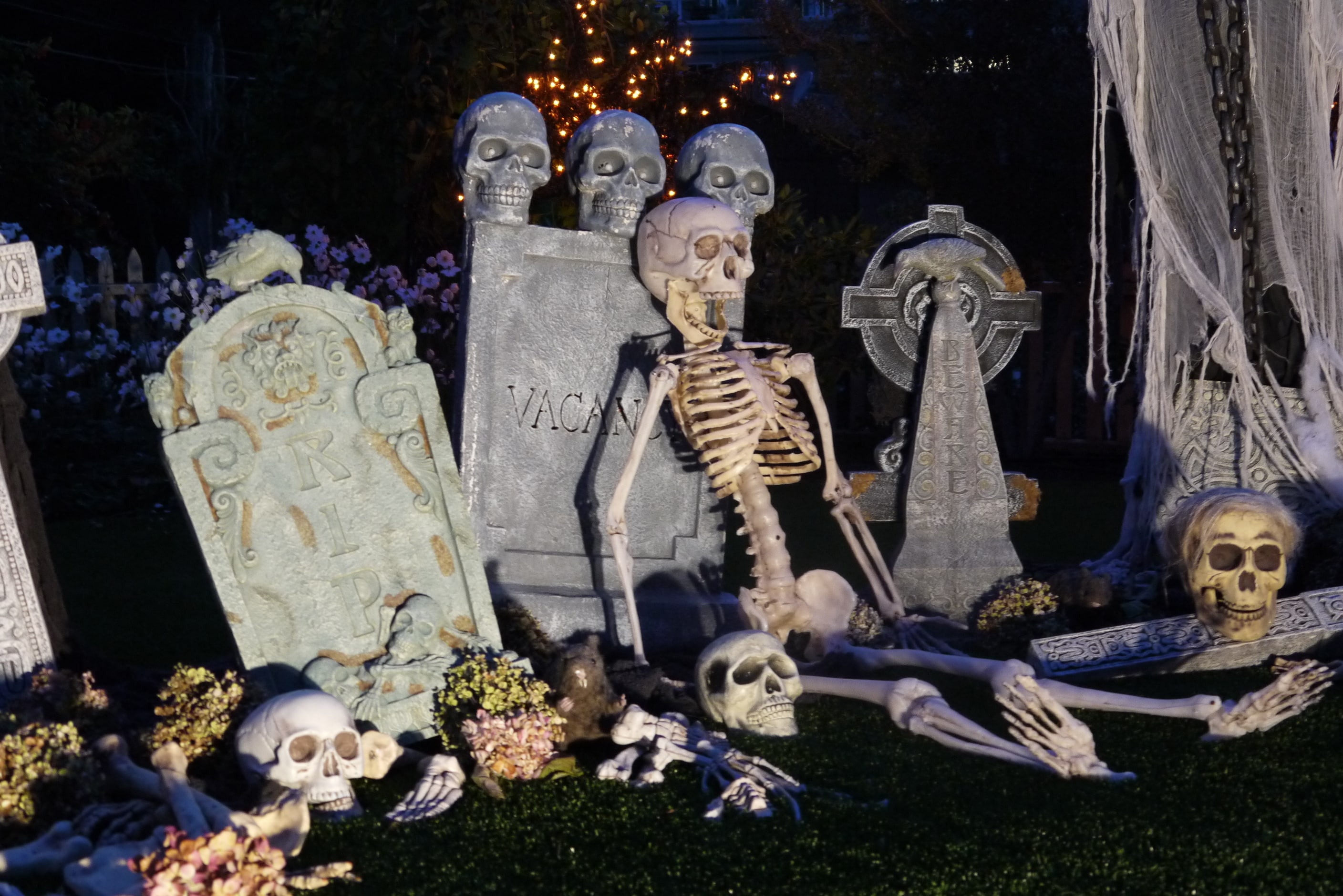 halloween decor skeletons leaning up against decorative tombstones in a graveyard scene at night