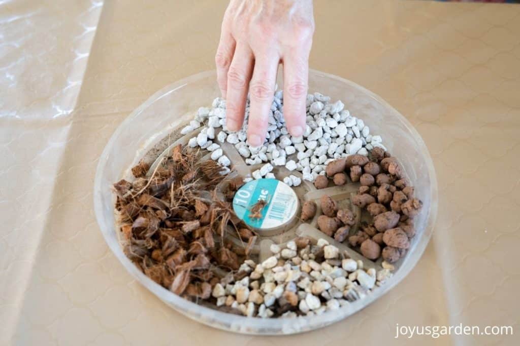 a hand hovers over a plastic saucer full of amendments to lighten succulent soil