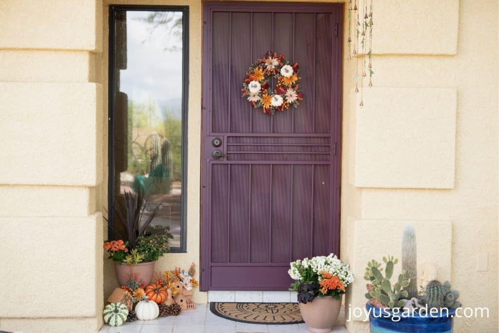 a front porch with flowers, a fall wreath, a bale of hay, birdhouse, fake pumpkins, gourds, and pinecones