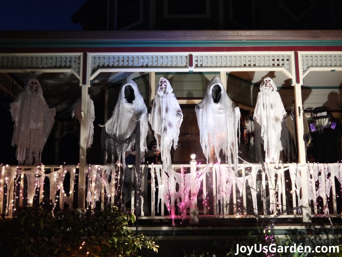 Exterior of house shown with front porch decorations of hanging ghosts at night.
