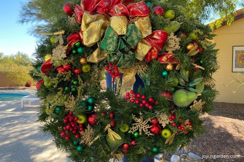green christmas wreath with golden ornaments red berries red gold and green ribbon and green apples and pears
