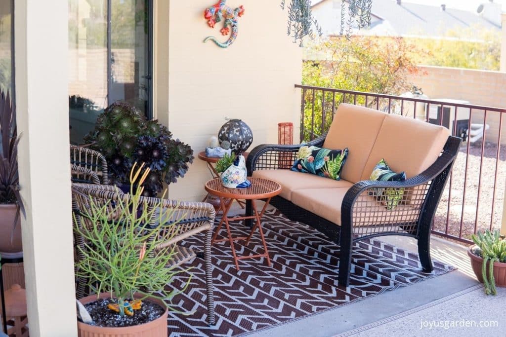 the seating area of a patio with a seating seat, loveseat, small tables, & plants