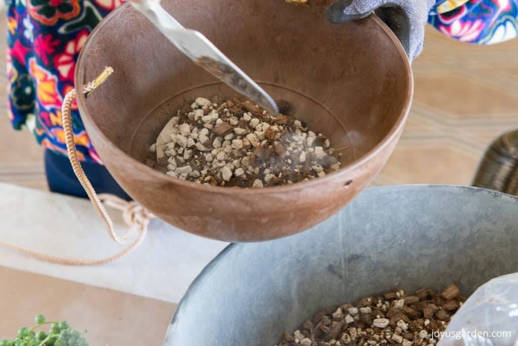 a terracotta colored hanging pot is getting a layer of succulent & cactus mix placed into the bottom