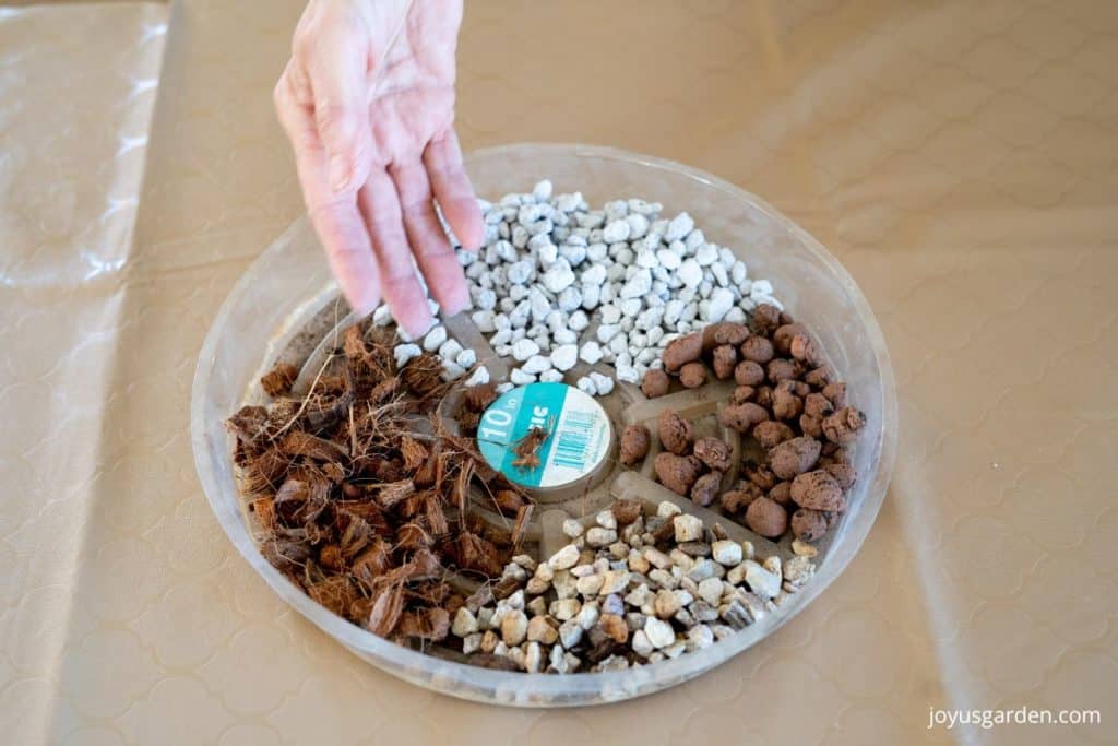 a hand hovers above a plastic plant saucer filled with amendments to add aeration & drainage to cactus soil