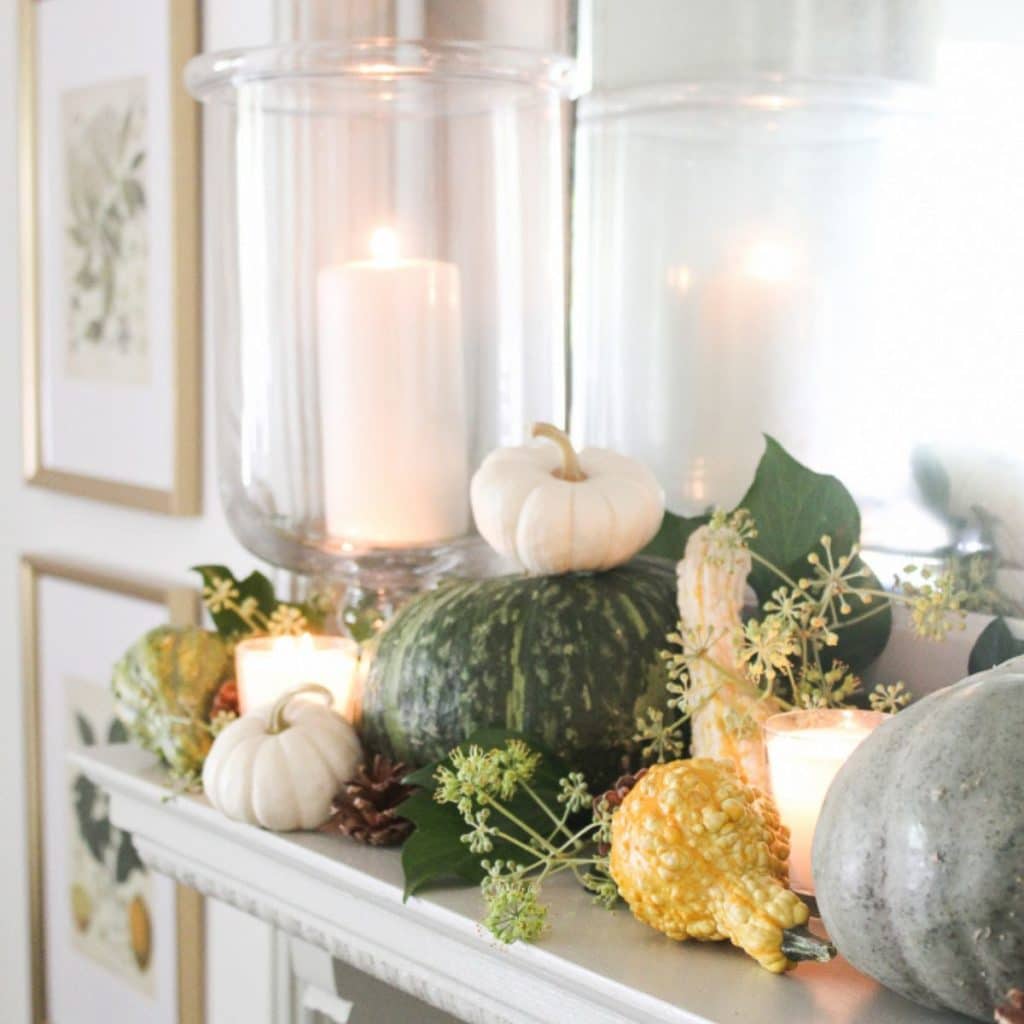 a fall display on a mantle with green, white, & orange squashes & candles