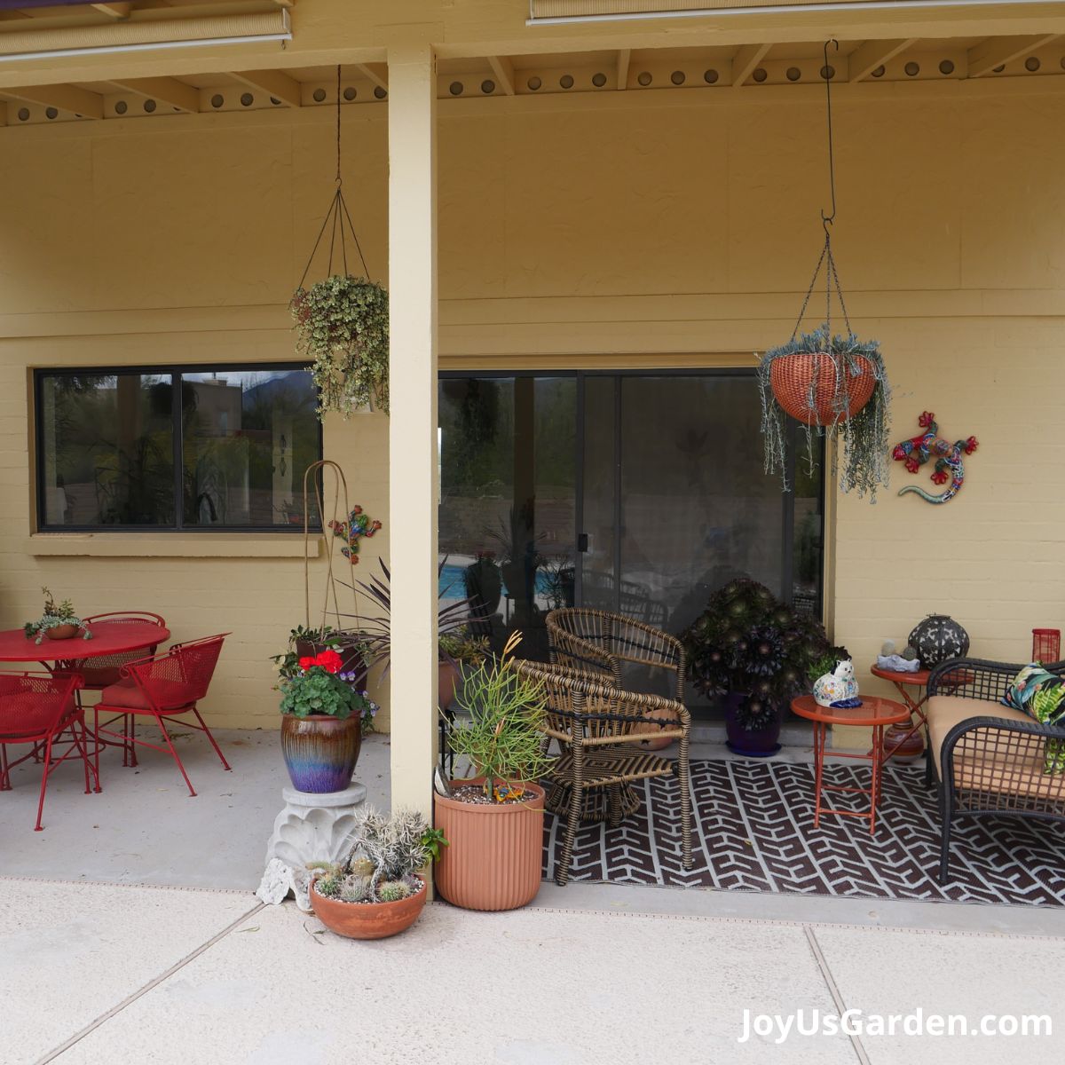 back patio shown with table and chairs and additional chair seating, a variety of flowers, cactus, and succulents potted and hanging