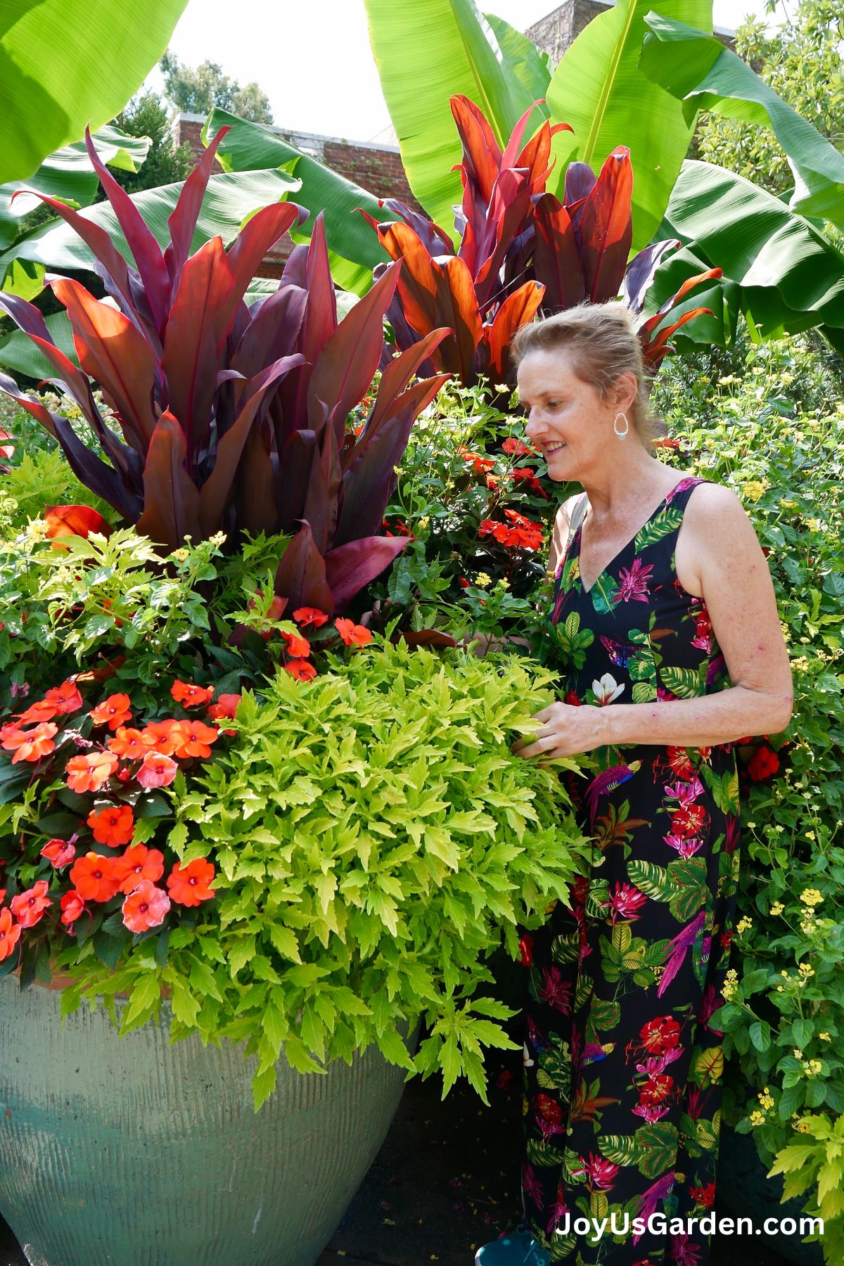 nell foster at atlanta botanical gardens in a tropical print jumpsuit standing next to a large pot of impatiens and a variety of plants