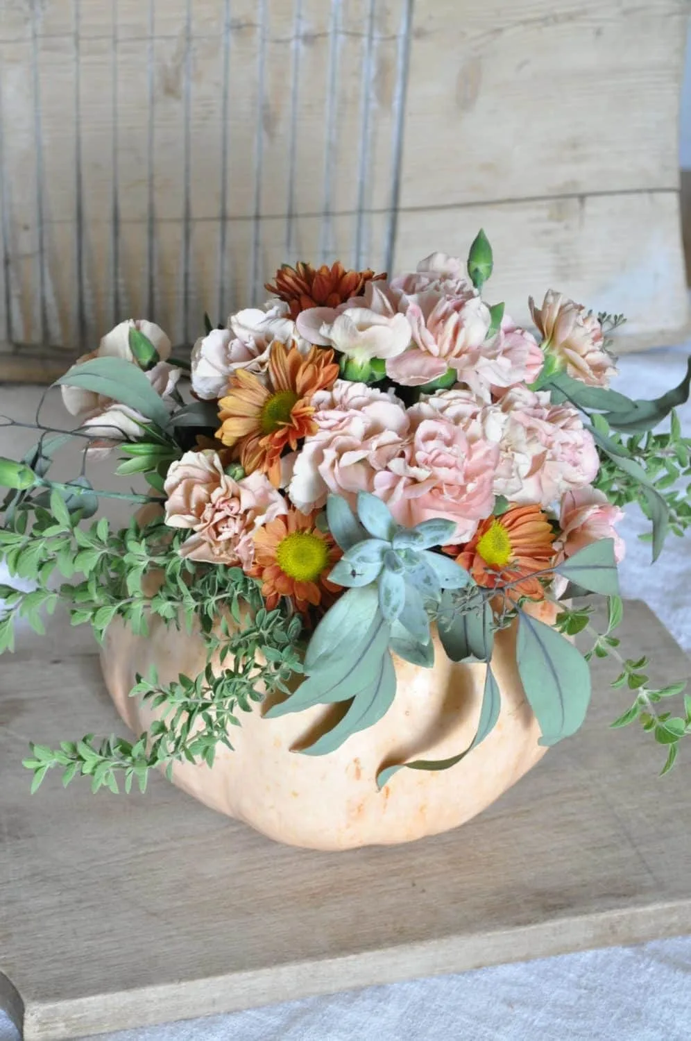 Pastel flowers, succulent stems, & herb stems decorate a light pink pumpkin for fall.