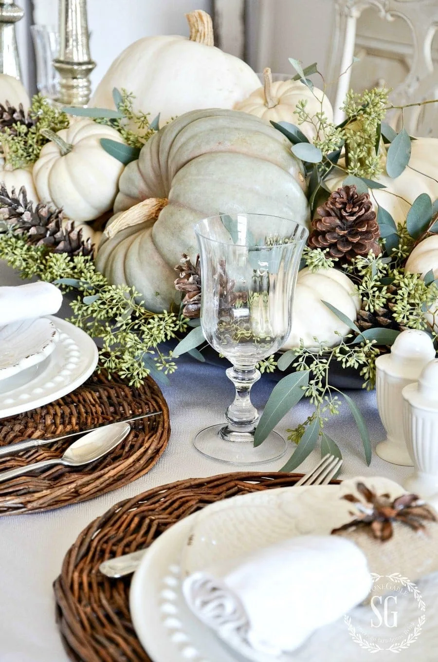 A fall centerpiece with greens pumpkins, white pumpkins, pine cones & eucalyptus.