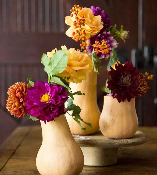 Jewel tone fresh flowers sit in butternut squashes for a colorful fall centerpiece.