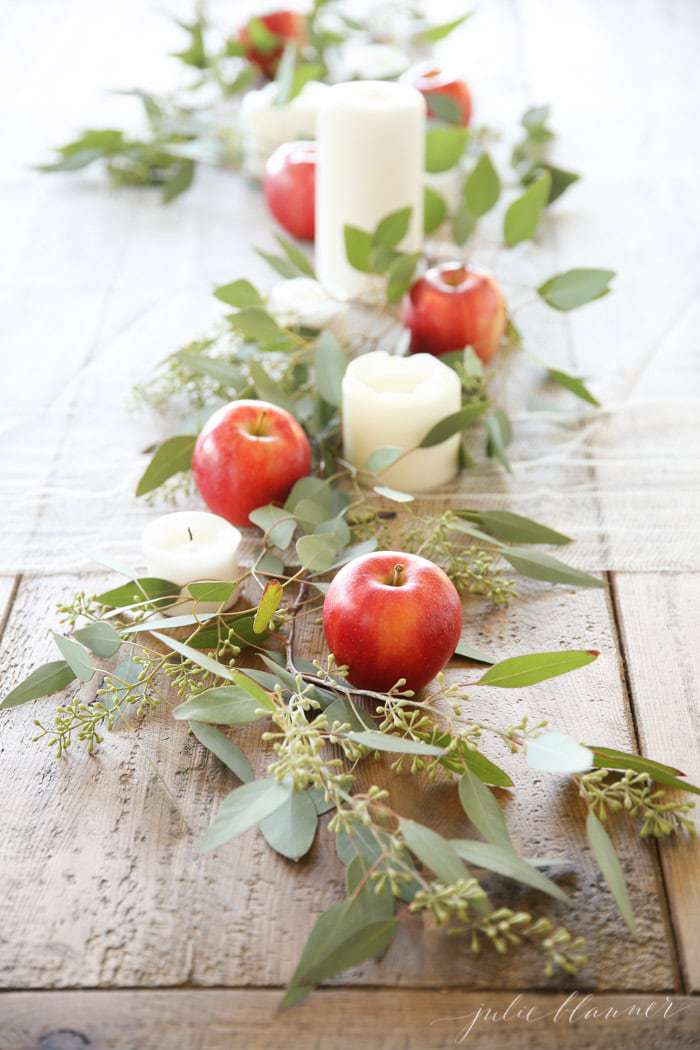 A simple fall centerpiece with red apples, white candles, & seede eucalyptus.