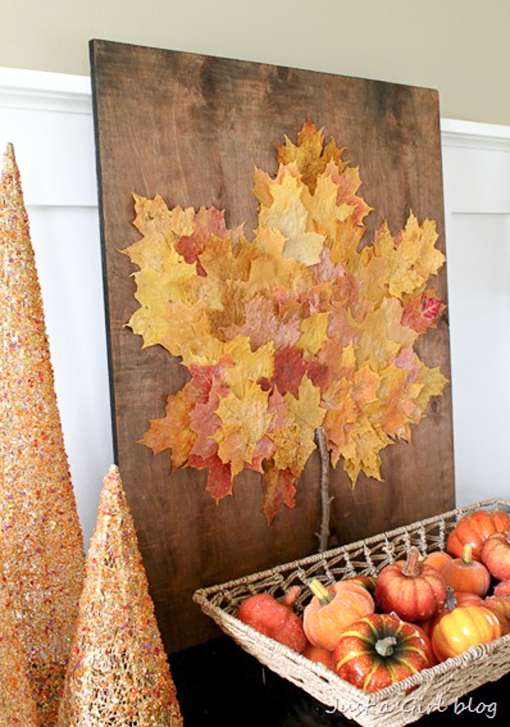 A board adorned with leaf art diy sits on a table with fall glitter trees & a basket of mini pumpkins.