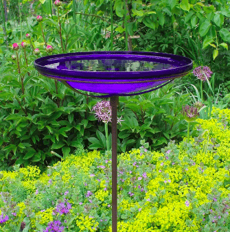 Cobalt blue glass bird bath is shown in a flower garden from etsy.