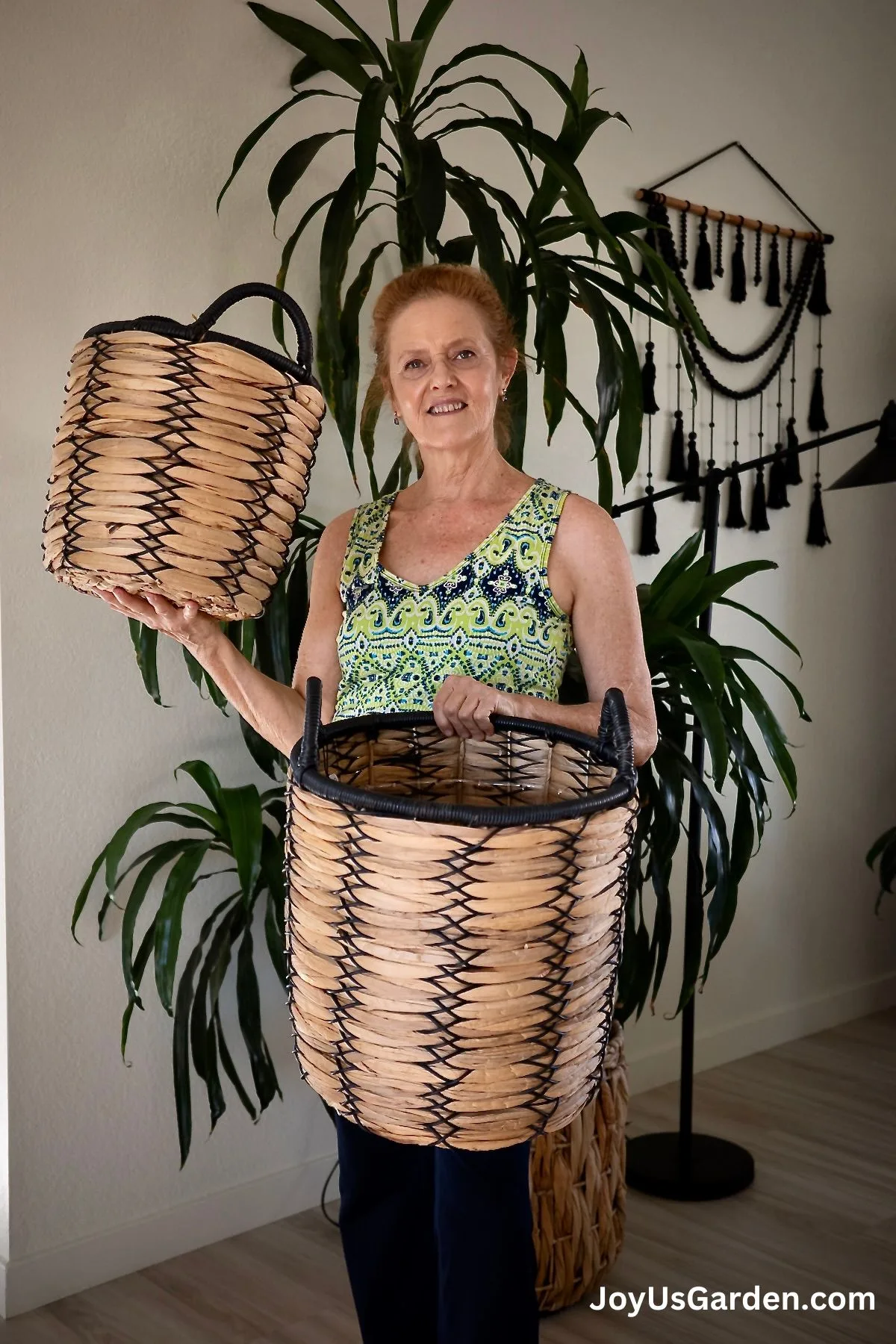 Nell Foster stand in front of dracaena lisa holding 2 large plant baskets.